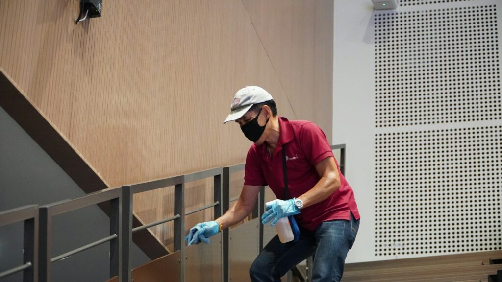Commercial cleaner in a face mask wiping a handrail in a modern building